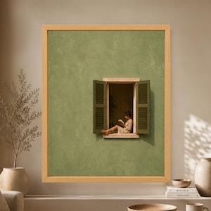 Framed minimalist sage green wall art showing a woman quietly reading inside a small open window with dark olive shutters and warm Mediterranean sunlight.