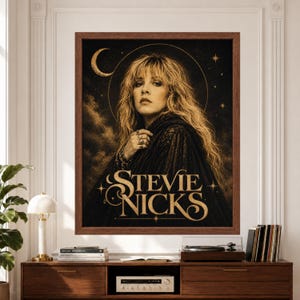 Framed Stevie Nicks wall art featuring a vintage-inspired rock portrait in black and gold with flowing blonde hair, crescent moon, celestial stars and large ornate “Stevie Nicks” typography above a record player console.