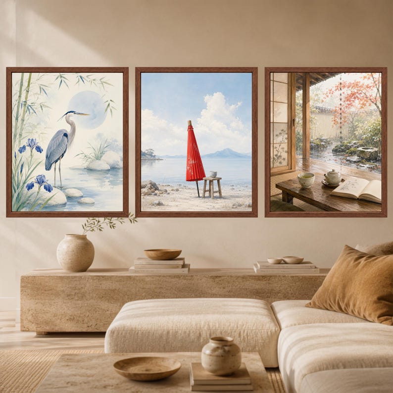 May include: A set of three framed wall art prints. The left print shows a blue heron near bamboo and irises. The center print depicts a red parasol on a beach. The right print shows a wooden table with a tea set and an open book by a window.