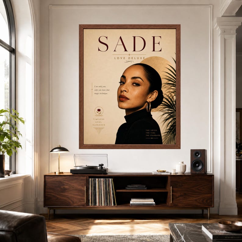 May include: A framed wall art print featuring a portrait of Sade with the text SADE LOVE DELUXE, a palm leaf silhouette, and a golden circle. The poster includes small text elements and a floral icon on a beige background, encased in a brown frame.