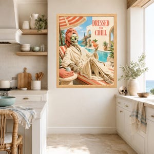 May include: A framed wall art print featuring a skeleton wearing a beige bathrobe, a matching head towel, and cucumber slices over its eyes. The skeleton reclines on a lounge chair by a pool, holding a cocktail, with the text DRESSED TO CHILL.