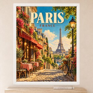 May include: A framed wall art print featuring a Parisian street scene with a cafe, red-checkered tablecloths, a black bicycle, and the Eiffel Tower in the distance. The text PARIS FRANCE is printed in large, bold, cream-colored letters at the top.