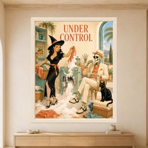 Framed Under Control wall art showing a retro witch beside an overflowing mint washing machine while a skeleton drinks tea and a black cat sits on folded towels in a sunny Mediterranean laundry room.