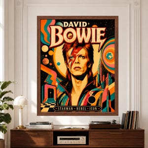 Framed David Bowie wall art featuring Bowie with lightning-bolt makeup surrounded by bold orange and teal retro graphics, planets, stars, geometric city shapes and Starman Rebel Icon typography.