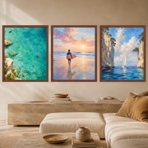 May include: A set of three framed wall art prints featuring coastal scenes. The left print shows an aerial view of turquoise water with swimmers. The center print depicts a person with a surfboard on a beach at sunset. The right print shows a sailboat between cliffs.