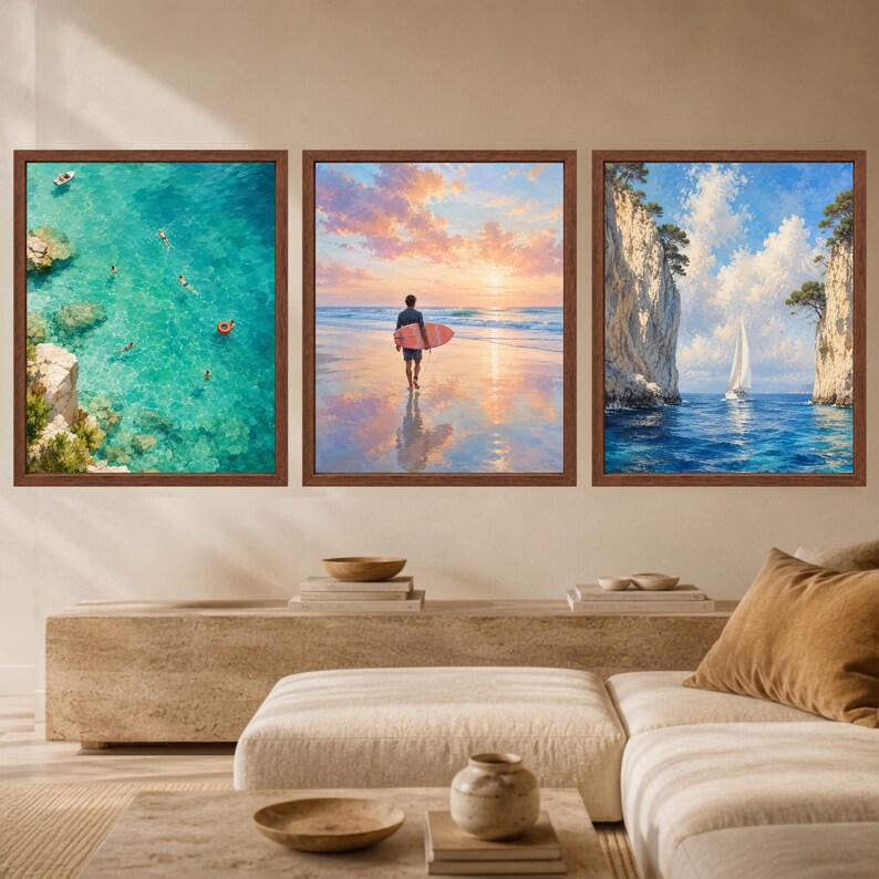 May include: A set of three framed wall art prints featuring coastal scenes. The left print shows an aerial view of turquoise water with swimmers. The center print depicts a person with a surfboard on a beach at sunset. The right print shows a sailboat between cliffs.