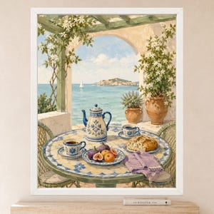 May include: A framed painting depicting a Mediterranean terrace with a tiled table set for tea. The table holds a blue and white teapot, two matching cups, a plate of figs and peaches, a loaf of bread, and a purple napkin. A sailboat is visible at sea.