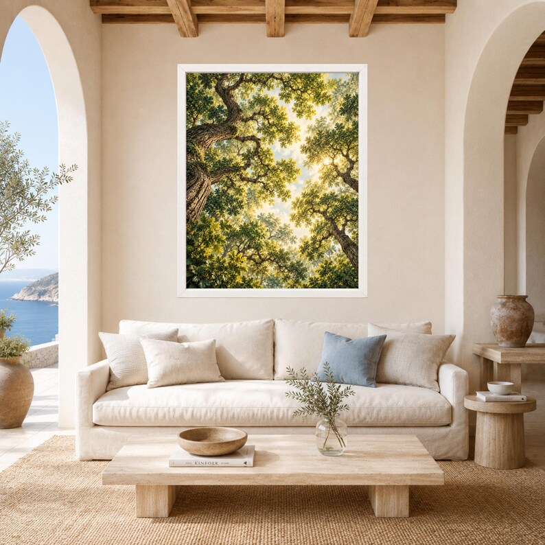 May include: A framed wall art print featuring a low-angle view of a lush forest canopy with sunlight filtering through green leaves and textured tree trunks. The artwork is displayed in a white frame above a beige sofa with decorative pillows.