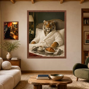 May include: A large framed wall art print featuring a tiger wearing a white bathrobe, sitting in bed with a silver tray holding a cup of coffee and a croissant. To the left, a smaller framed print shows a black cat sitting at a wooden counter.