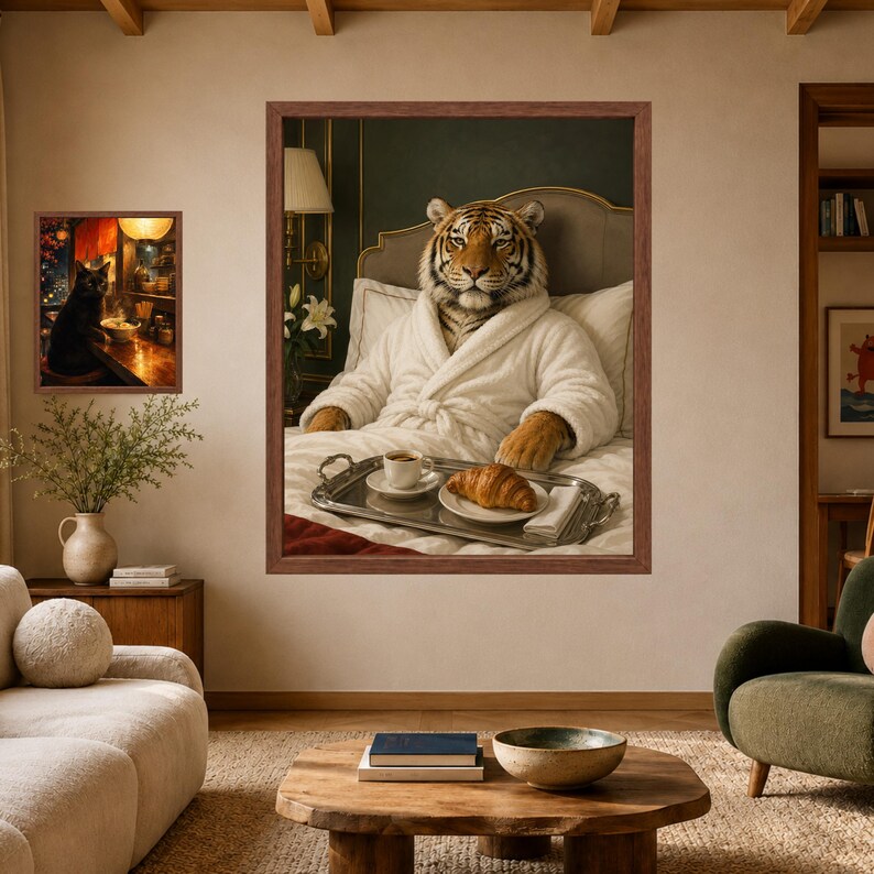 May include: A large framed wall art print featuring a tiger wearing a white bathrobe, sitting in bed with a silver tray holding a cup of coffee and a croissant. To the left, a smaller framed print shows a black cat sitting at a wooden counter.