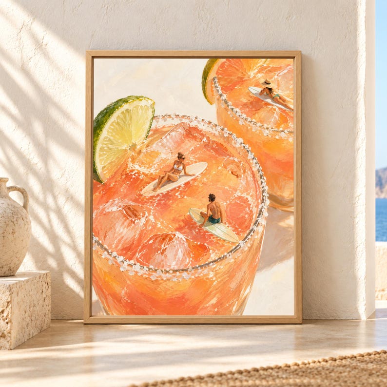 Framed cocktail wall art showing oversized coral margarita-style drinks with salted rims, ice and lime wedges while tiny surfers relax on surfboards floating inside the glasses.