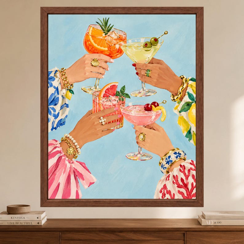 May include: A framed art print depicting four hands raised in a toast, each holding a different cocktail. The drinks include an orange spritz, a martini with olives, a grapefruit drink, and a pink cocktail with cherries, all against a light blue background.