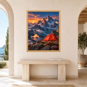 May include: A framed wall art print featuring a vibrant orange tent perched on a rocky mountain ledge overlooking a lake. The scene captures snow-capped peaks under a dramatic sunset sky with clouds glowing in shades of orange, pink, and deep blue.