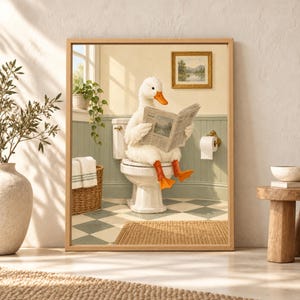 Framed funny duck bathroom wall art showing a white duck sitting on a toilet and reading a newspaper in a sunny sage green bathroom with checkerboard flooring, towels and plants.