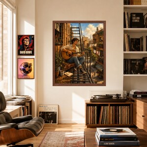 May include: A framed wall art print depicting a person sitting on a metal fire escape playing an acoustic guitar. The scene shows an urban apartment building exterior with laundry hanging, a potted plant, and a book nearby under a blue sky.