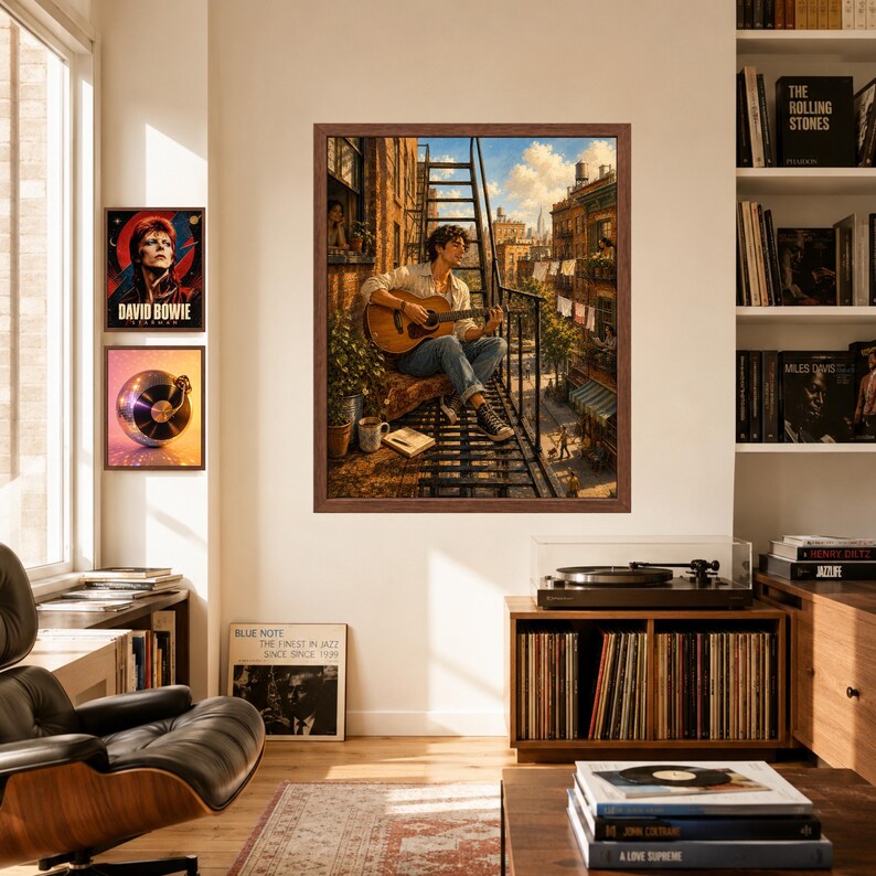 May include: A framed wall art print depicting a person sitting on a metal fire escape playing an acoustic guitar. The scene shows an urban apartment building exterior with laundry hanging, a potted plant, and a book nearby under a blue sky.
