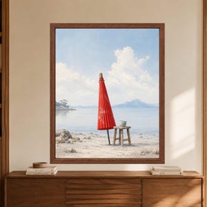Framed Japanese red umbrella wall art showing a closed red wagasa beside a small wooden stool with a tea cup on a pale beach with calm blue water, distant mountains and soft clouds.