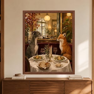 Framed whimsical animal wall art showing a greyhound and red fox sharing a candlelit restaurant dinner with red wine, plated food and bread in an elegant burgundy and brass dining room.