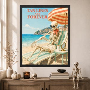 May include: A framed wall art print featuring a skeleton wearing sunglasses and a red neckerchief, lounging on a striped beach chair under a red and white umbrella. The text TAN LINES ARE FOREVER is printed in red above the beach scene.
