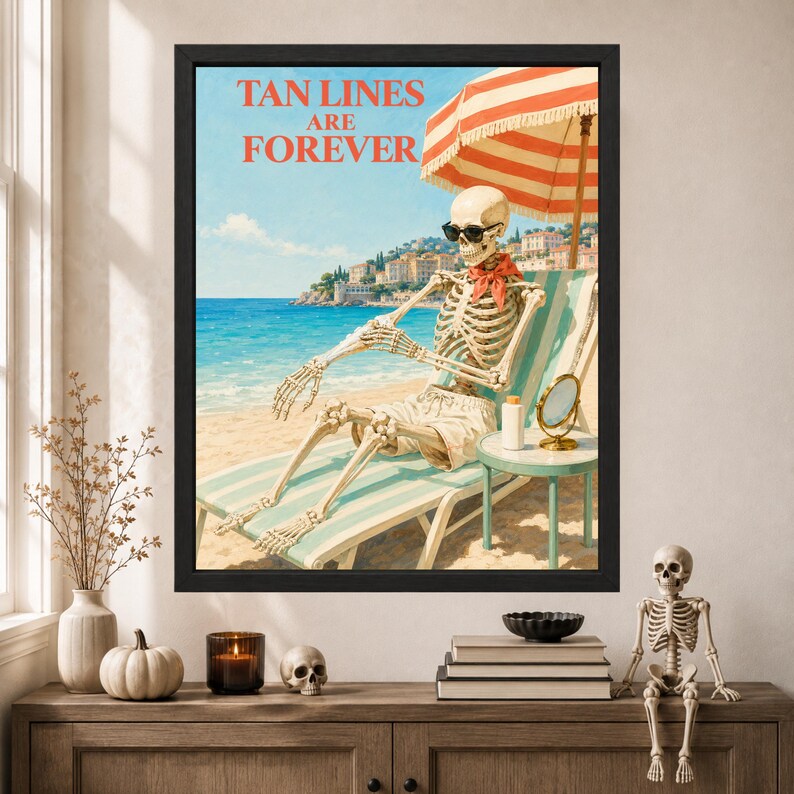 May include: A framed wall art print featuring a skeleton wearing sunglasses and a red neckerchief, lounging on a striped beach chair under a red and white umbrella. The text TAN LINES ARE FOREVER is printed in red above the beach scene.