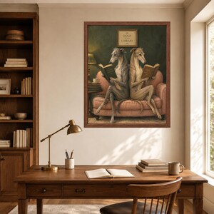 May include: A framed wall art print titled Dogs of the Library featuring two greyhounds sitting on a pink sofa, each reading a book. The artwork is displayed in a dark wood frame and depicts the dogs in a library setting with a small table and lamp.