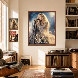 Puede incluir: Una impresi&oacute;n de arte de pared enmarcada que muestra un retrato de Stevie Nicks cantando en un micr&oacute;fono, con cabello rubio largo y una prenda fluida. El texto STEVIE NICKS est&aacute; impreso en letras doradas en el centro inferior, en un marco marr&oacute;n.