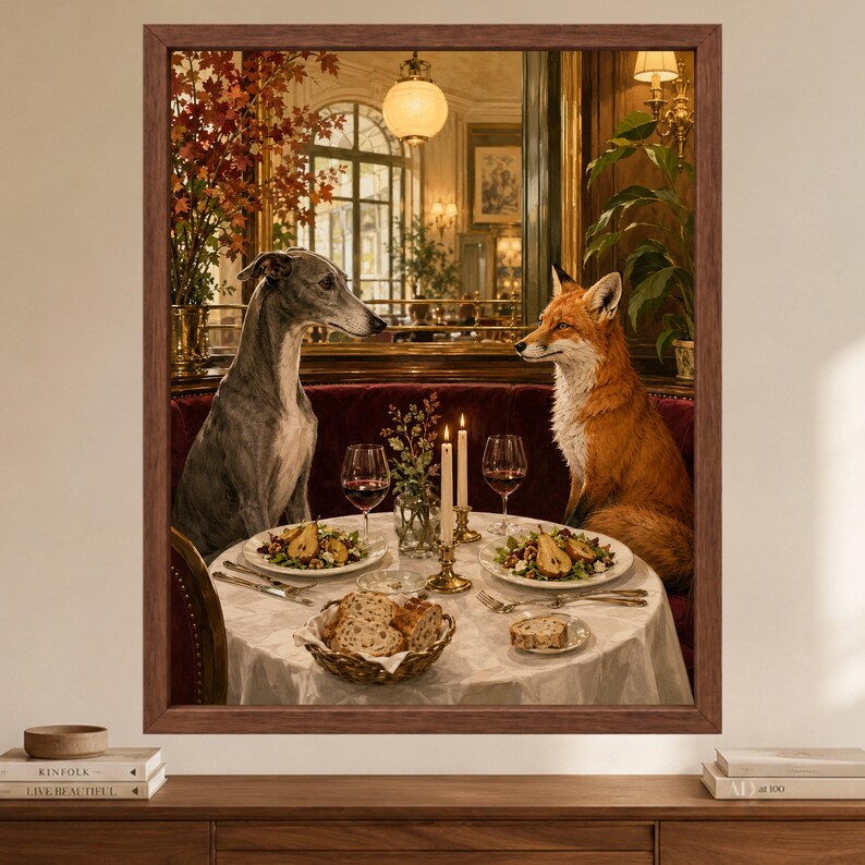May include: A framed wall art print depicting a grey whippet and a red fox sitting opposite each other at a round table in a restaurant. The table is set with two plates of food, wine glasses, candles, and a basket of bread on a white cloth.