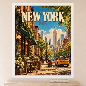 May include: A framed wall art print depicting a New York City street scene with the text NEW YORK USA at the top. The image shows a sidewalk cafe with green awnings, tables, and chairs, a yellow taxi on the road, and the Empire State Building.