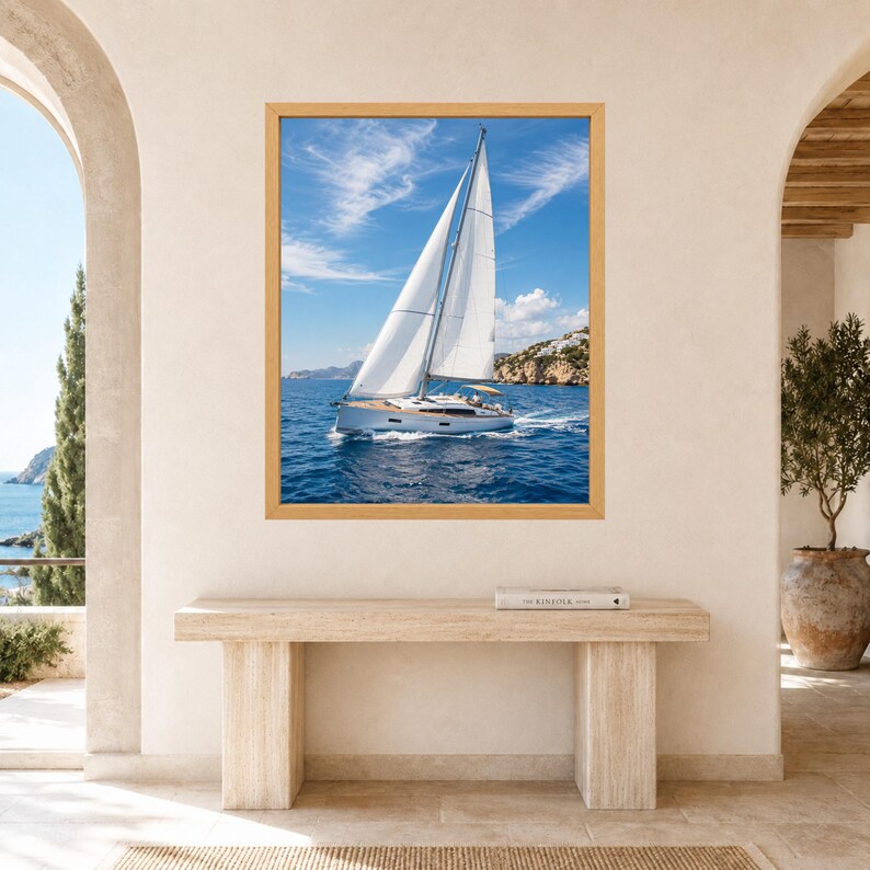 Puede incluir: Una impresi&oacute;n de arte mural enmarcada que muestra un velero blanco con una vela grande navegando por aguas oce&aacute;nicas de color azul profundo bajo un cielo brillante con nubes tenues, con una costa rocosa visible a la derecha.