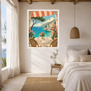 May include: A framed wall art print depicting a coastal Mediterranean scene with a round table set for two under a striped awning. The view features a turquoise sea, distant white buildings on a cliffside, and vibrant pink geraniums in the foreground.