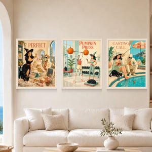 May include: Three framed wall art prints featuring retro-style illustrations. The first shows a witch and a skeleton baking with the text PERFECT. The second shows a skeleton and a witch at a gym with the text PUMPKIN PRESS. The third shows a witch and a skeleton fishing with the text CASTING CALL.