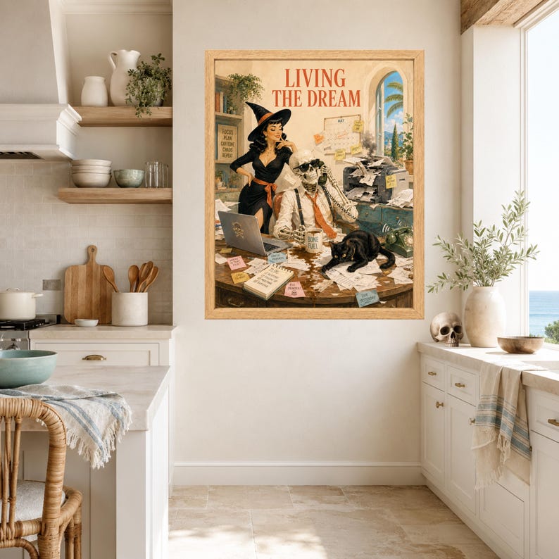 May include: A framed wall art print titled LIVING THE DREAM, depicting a witch in a black dress and a skeleton in a white shirt and tie working at a cluttered desk with a black cat, a laptop, a printer, and scattered papers in an office setting.