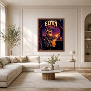 May include: A framed wall art print featuring a stylized illustration of Elton John playing a piano. The artwork displays the text ELTON JOHN in bold lettering above the musician, set against a vibrant purple and orange sunset background.