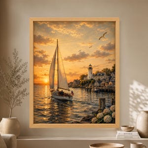 Framed New England coastal wall art showing a sailboat crossing a golden sunset harbor beside a white lighthouse, shingled seaside cottages, docks, hydrangeas and flying seagulls.