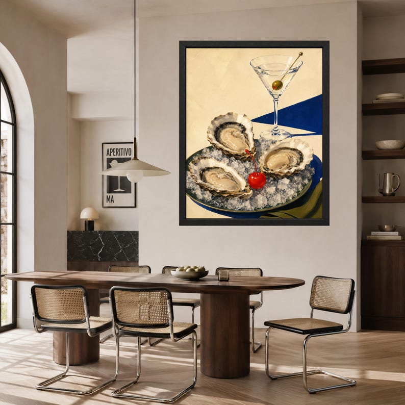 May include: A framed wall art print featuring three raw oysters served on a bed of crushed ice on a plate, accompanied by a single bright red cherry and a clear martini glass containing a green olive, set against a cream and blue background.