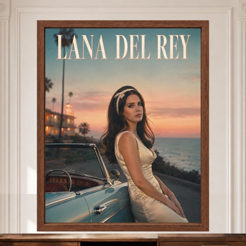 May include: A framed wall art print featuring Lana Del Rey in a cream-colored sleeveless dress and a white headband, leaning against a light blue vintage car. The background shows a sunset over the ocean with palm trees and a building.