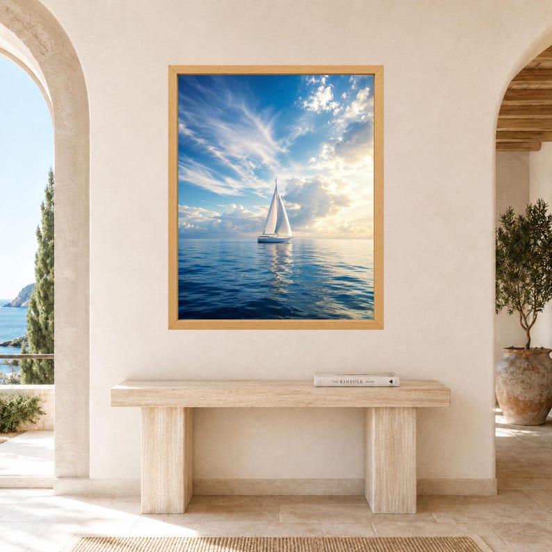 Pode incluir: Uma impress&atilde;o de arte de parede retangular apresentando um veleiro branco em um oceano calmo e azul profundo sob um c&eacute;u brilhante com nuvens finas e luz solar dourada. A obra est&aacute; em uma moldura de madeira clara em uma parede neutra.
