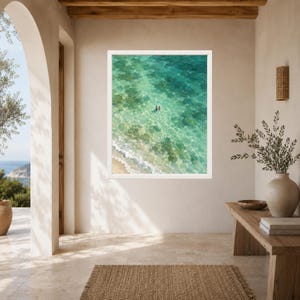 May include: A rectangular framed wall art print featuring an aerial view of a turquoise ocean with clear shallow water, a sandy shoreline with white waves, and two small figures swimming in the center of the vibrant, sunlit sea.