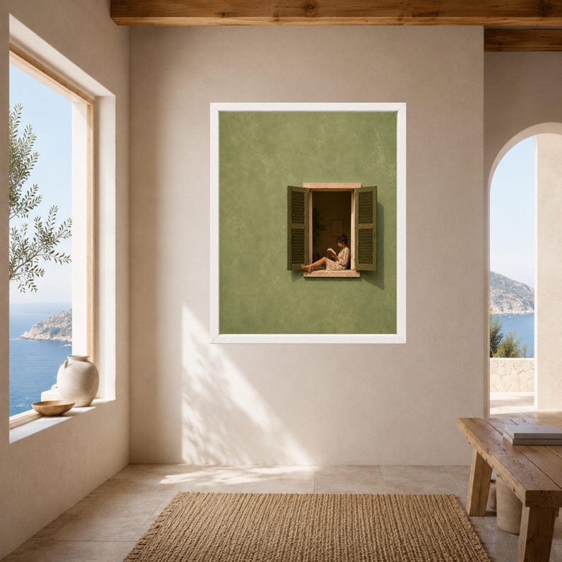 May include: A framed wall art print featuring a sage green wall with an open window. The window has dark green shutters and shows a person sitting on the ledge reading a book. The artwork is displayed in a white frame on a neutral wall.