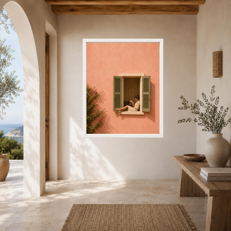 May include: A framed wall art print featuring a peach-colored exterior wall with an open window. Green shutters frame the window, where a person sits reading. The scene includes a climbing vine on the left side of the wall, creating a warm, sunlit aesthetic.
