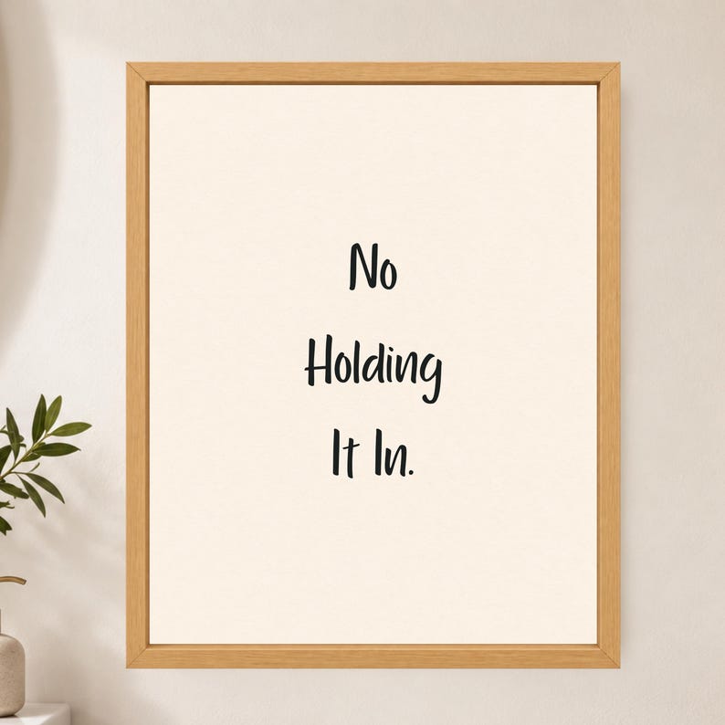 May include: A framed wall art piece featuring a light cream background with the black text No Holding It In centered in the middle. The artwork is enclosed in a simple, light-toned wooden frame with a clean, rectangular profile and smooth finish.