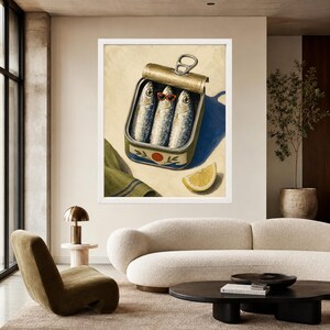 May include: A framed wall art print depicting an open metal tin containing three sardines, with the center fish wearing small red-rimmed sunglasses. A single lemon wedge sits nearby, and a green cloth with blue stripes is visible in the corner.