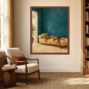 May include: A framed wall art print featuring a leopard resting on a yellow curved chaise lounge in a room with deep teal walls and a stone floor. A small red book sits on the lounge, and a palm tree is visible through an open doorway.