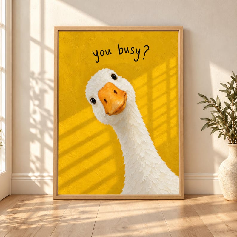 Framed funny goose wall art showing a white goose tilting its head toward the viewer beneath handwritten “you busy?” text on a textured yellow background.