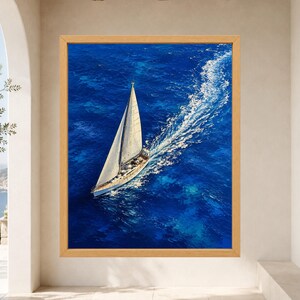May include: A framed wall art print featuring an aerial view of a white sailboat navigating deep blue ocean waters. The vessel leaves a prominent white wake behind it, contrasting with the vibrant, textured shades of blue in the sea.