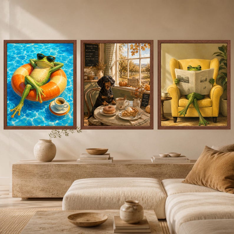 May include: A set of three framed wall art prints. The left print shows a frog in sunglasses on an orange pool float. The centre print features a dachshund at a table with a donut. The right print depicts a frog reading a newspaper in a yellow chair.