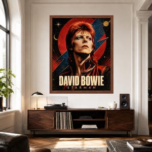 May include: A framed wall poster featuring a portrait of David Bowie with red hair and a gold circular emblem on the forehead. The background displays a large red circle, a blue lightning bolt, and celestial elements. The text reads DAVID BOWIE STARMAN.