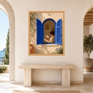 May include: A framed wall art print featuring an arched window with vibrant blue shutters set into a beige stucco wall. Inside the window, a person sits reading a book. The scene includes a terracotta pot with an olive tree and blue flowers.