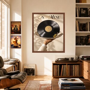 May include: A framed wall art print titled On The Menu featuring a black vinyl record served on a silver platter held by a hand in a white sleeve, with a green olive garnish. The print is displayed in a room with a record player and books.