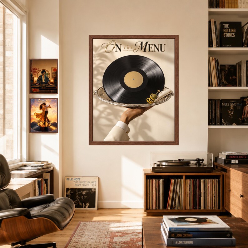 May include: A framed wall art print titled On The Menu featuring a black vinyl record served on a silver platter held by a hand in a white sleeve, with a green olive garnish. The print is displayed in a room with a record player and books.